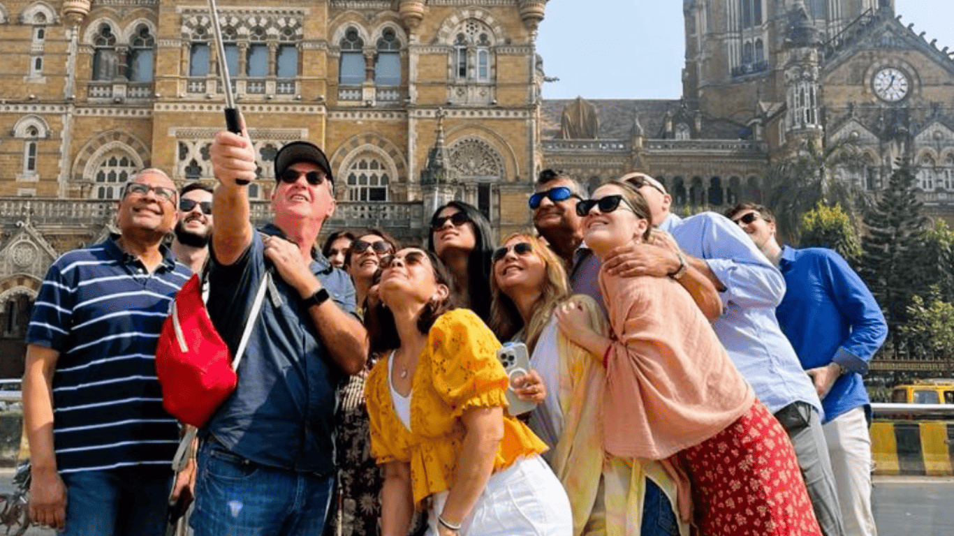Group of international travelers taking a selfie together in front of Chhatrapati Shivaji Maharaj Terminus during a Mumbai city tour.